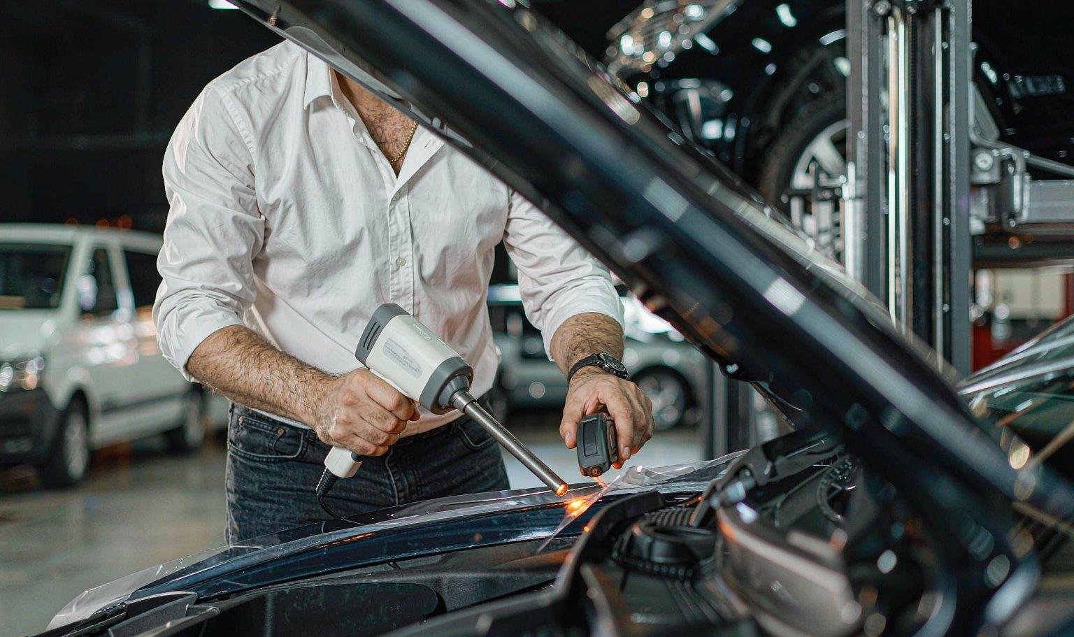 Installer post-heating a Clear TPU PPF edge on a car hood with an IR thermometer in a clean workshop