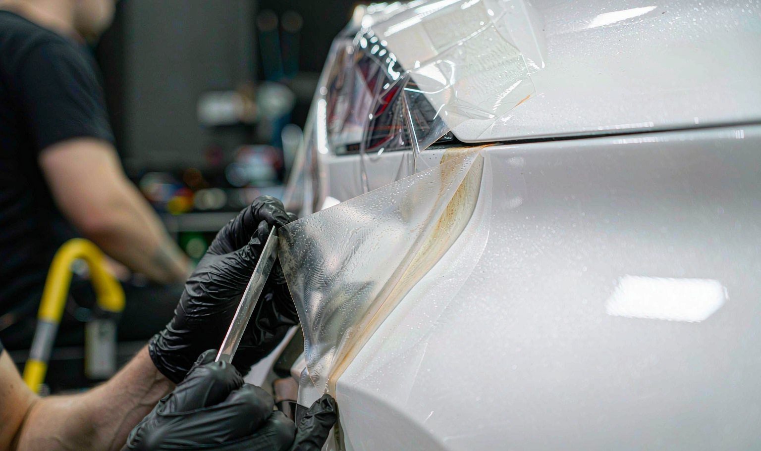 Installer lifting the edge of yellowed TPU PPF film from a white car fender to document a warranty claim