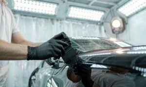 Installer in nitrile gloves laying gloss black Car Wrap Vinyl across a door panel inside a filtered wrap booth